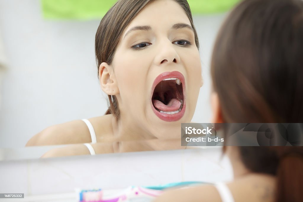 Pain in throat. Young beautiful woman is openning her mouth and looking in mirror, in bathroom, in home. Ill throat's concept. Mouth Open Stock Photo