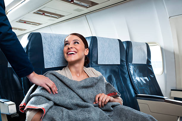 On the airplane A cheerful young woman sitting on the airplane thanks an air stewardess for a blanket. airplane interior stock pictures, royalty-free photos & images