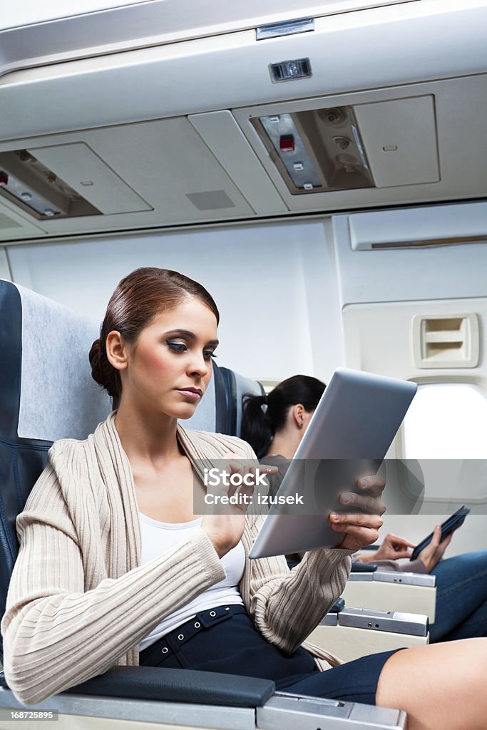 During the flight Young woman sitting on the airplane and using a digital tablet. Adult Stock Photo