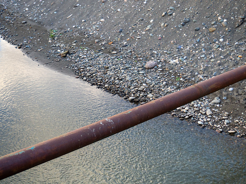 pipe runs over the river. Rusty pipe. Water surface. Pebble bank of the river and sea