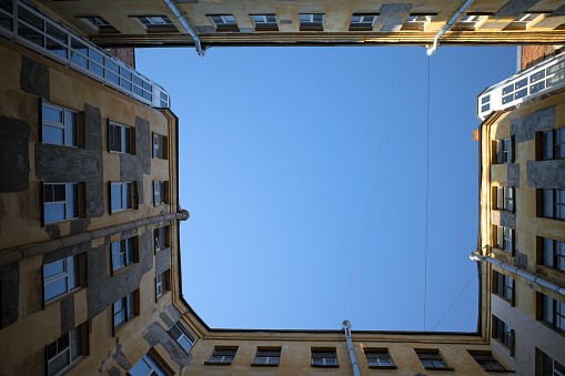 Bottom up view of unusual old house yard well in St. Petersburg, Russia. Wall, windows and little part of blue clear sky