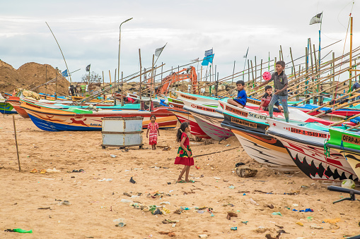 Beruwala, Sri Lanka 03 February 2023. Fishing boats stand in Beruwala Harbour. bright colored traditional sri lankan fishing boats stand on yellow sandy ocean shore. local children play near boats