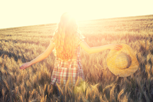 woman  in a wheat field holding hat