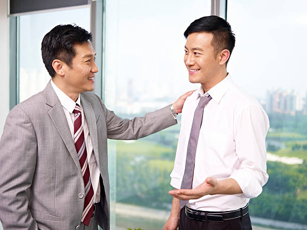 asian business people asian businessman standing and talking by the windows in office.  subordination stock pictures, royalty-free photos & images