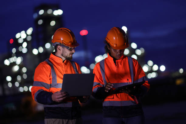 istock A couple of Electrical engineers with red safety jackets and hard hats using tablets and laptops working at a front factory on night shift. 1687319430