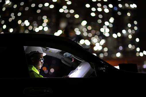 Female system engineer wearing a green safety uniform and hard work in the car with the drawing against bokeh background