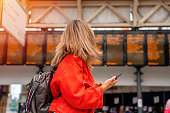 asian woman with backpack and holding smartphone while at the train station and the train is arriving., Enjoying travel concept