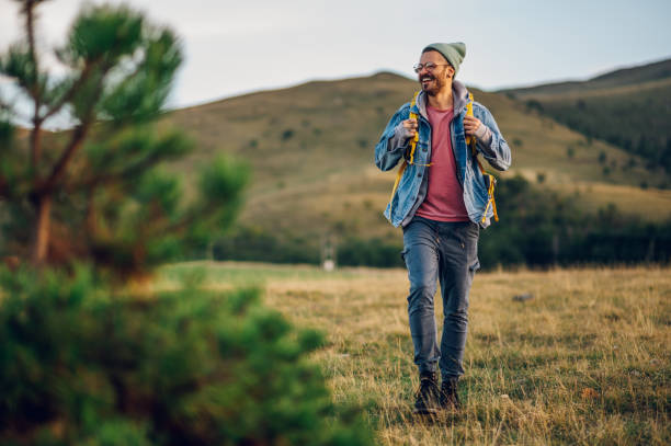 Portrait of a stylish man hiking on a mountain path with tall grass Portrait of a caucasian stylish man in warm clothes hiking in mountains and enjoying adventure on a vacation. Active fit lifestyle. Smiling fashionable male spending day in nature. Copy space. hot handsome man stock pictures, royalty-free photos & images