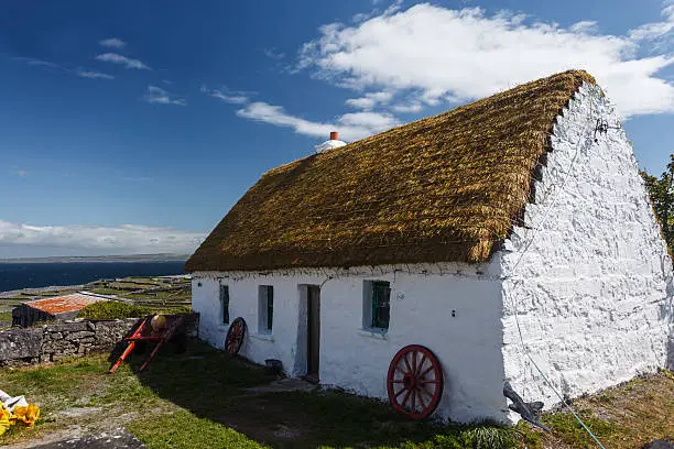 A neat whitewashed thatched roof Irish cottage on the island of Inishee  with wagon wheels and farm cart in front