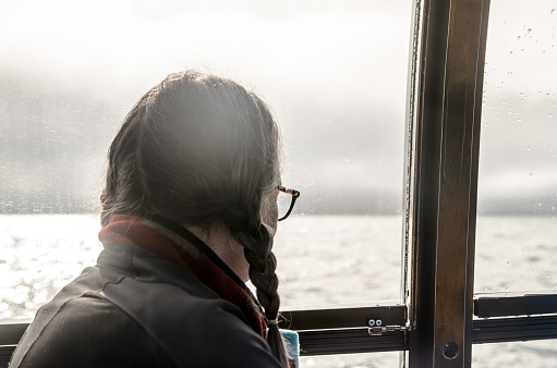 Headshot of woman looking for whales while being on a boat on St. Lawrence river during cloudy day of summer