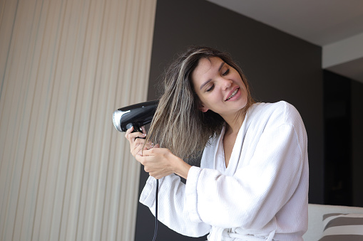 The beautiful woman in a bath towel using a hairdryer after showering in the Hotel room