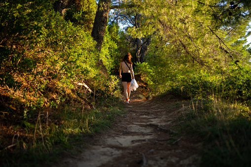 Rear view of a young caucasian woman walking in a sun-lit forest.