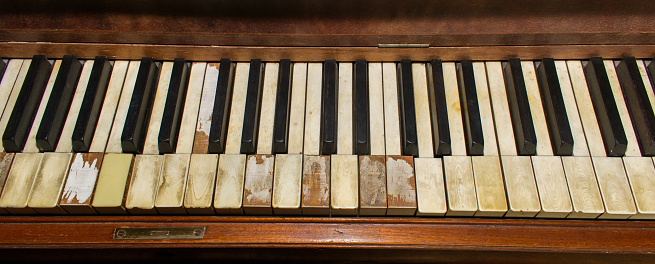Old wooden upright grand piano black and white keys with detailed real ivory inlays with some missing on late 1800s instrument, worn, broken, damaged and well played
