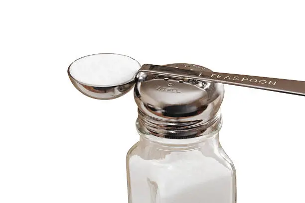 Teaspoon of salt resting on the top of salt shake. This is the recommended amount of sodium intake is less than one teaspoon healthy adults. Isolated on white with clipping path included.