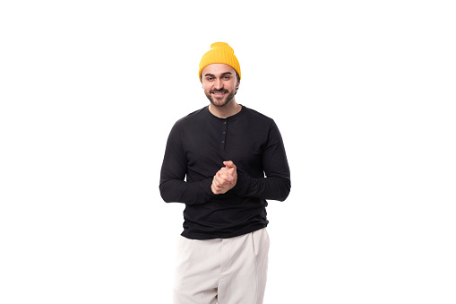 a young brutal male model dressed in a black jacket and a yellow cap looks friendly at the camera.