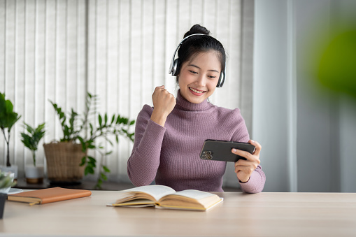 istock A cheerful Asian woman showing her fist and enjoying watching an online game show on her smartphone. 1687716415