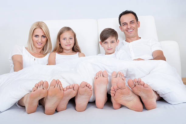 Happy Family In Bed Under Cover Showing Feet Happy Family With Two Children In Bed Under Cover Showing Feet, Indoors bed human foot couple two parent family stock pictures, royalty-free photos & images