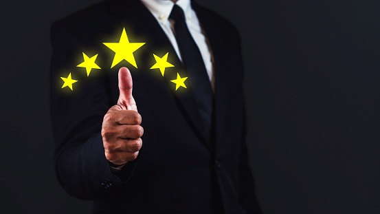 Customer satisfaction concept. Businessman is showing thumb up with five stars against dark blue background.