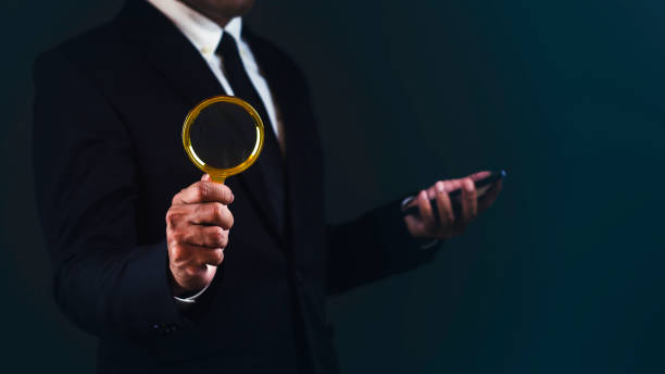 istock Businessman is using smartphone and magnifying glass searching for something against dark background. 1687761454