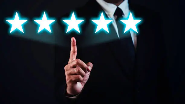 Photo of Businessman is showing index finger with five stars against dark background.