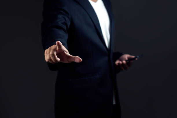 Businessman using a phone and pointing a finger against dark background.
