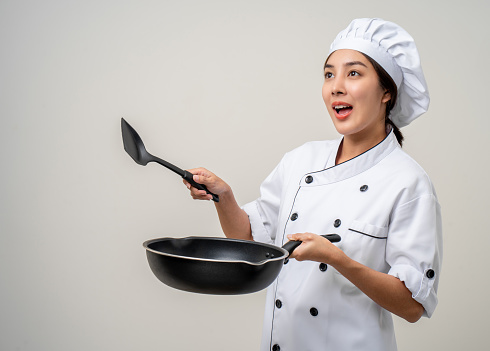 Young beautiful asian woman chef in uniform holding turner and iron Frying pan utensils cooking in the kitchen various gesture on isolated background. woman occupation chef restaurant and hotel.