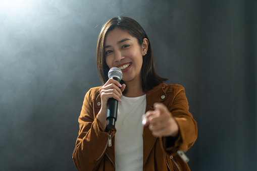 Attractive singer woman singing music on stage with spotlight strike through the darkness at concert event. Musician performing live with light in hall.