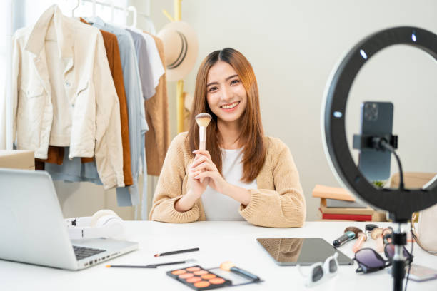 istock Young beautiful asian woman vlogger live broadcasting cosmetic makeup tutorial content with brush looking at camera. Influencers with various cosmetic recording video review sharing on social media 1687782838