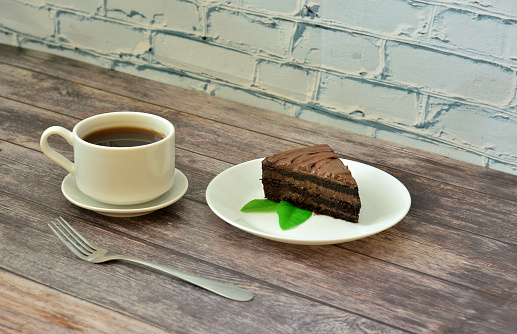 Delicious dessert, a piece of chocolate sponge cake with mint and a cup of hot black coffee on a wooden table. Close-up.