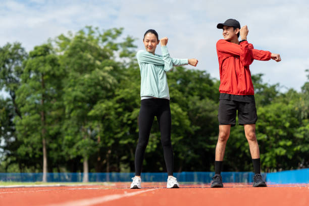 istock Couple asian jogging and running outdoors at sport stadium warming up stretching before workout. Happy healthy Man woman wearing sportswear jogging. Workout exercise Healthy and lifestyle. 1687790147
