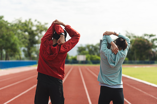 Couple asian jogging and running outdoors at sport stadium warming up stretching before workout. Happy healthy Man woman wearing sportswear jogging. Workout exercise Healthy and lifestyle.