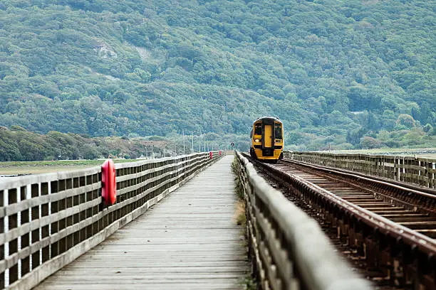 Wooden bridge with approaching train. Half is pedestrian and the other is a rail track.
