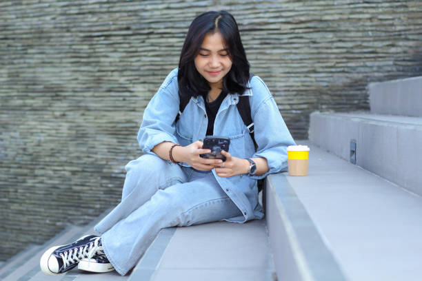 istock happy asian young woman using application on smartphone, watching video, surfing on social media networking and drink a cup of coffee while sitting in a mall stairs 1687892199