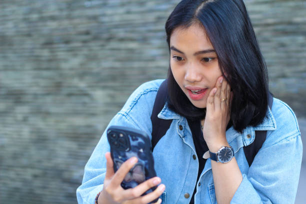 istock shocked asian young woman traveler smiling while using mobile application on smartphone, browsing social media, and watching video in urban outdoor 1687897391