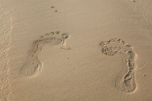 An attractive woman walks on a sandy beach leaving footprints in the sand, Tangalle, Sri Lanka