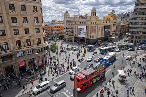 Gran Via street view, Madrid, Spain. Crowd of people at Callao Square and many cars including a tour bus in the street.