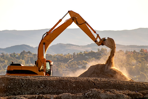 Backlit Backhoe scooping dirt  with hills in the background