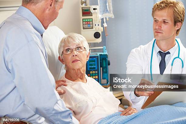 Doctor Hablando A Senior Pareja En Ward Foto de stock y más banco de imágenes de Mujeres - Mujeres, Serio, 80-89 años