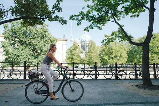 Woman cycling along Spree riverbank promenade in Berlin with cathedral and television tower in background, Germany
