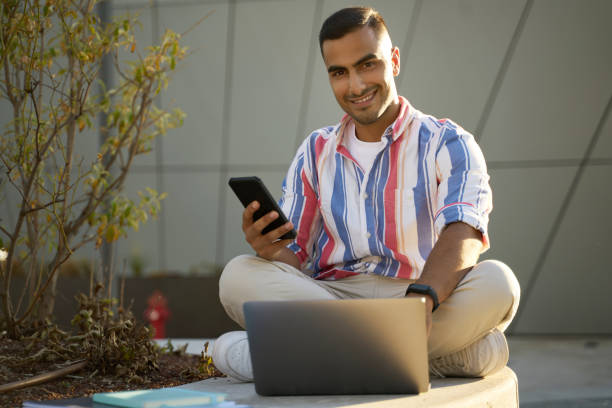 istock Smiling Iranian man freelancer holding smartphone using laptop working online at workplace 1688007011