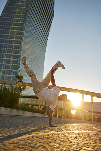 Young middle eastern man break dancing, standing on hand on urban street. Active lifestyle concept
