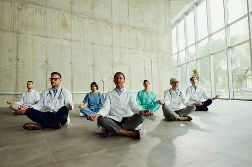 Large group of medical experts exercising Yoga in Lotus position on the floor in hospital. Copy space.