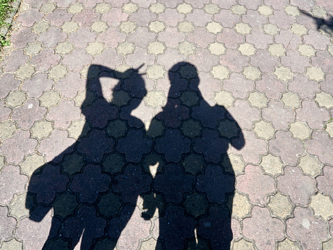Silhouette of a two people casting a shadow on a cobble stone road.