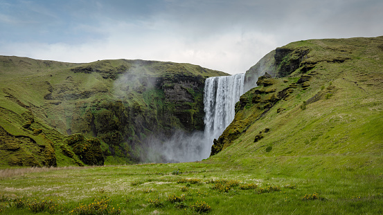 Iceland Skogafoss Waterfall under moody overcast cloudscape in summer. Falling water of the Skoga River. The Skógafoss is one of the biggest waterfalls in Iceland, with a width of 25m and a drop of 60m. Landscape Panorama over the surrounding green Nature. Skógar, Rangárþing eystra, Southern Iceland, Sudurland, Iceland, Nordic Countries, Europe