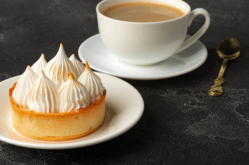 Meringue tart with coffee cup on dark gray background close up
