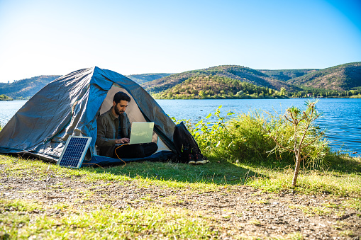 Young travel man relax and  using laptop computer work remotely anywhere using internet connected to portable solar panel charging