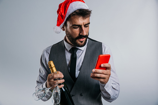 A suave, well-dressed man stands in the studio, his impeccable style complemented by a gleaming present in one hand and a smartphone in the other, as he revels in the holiday season.