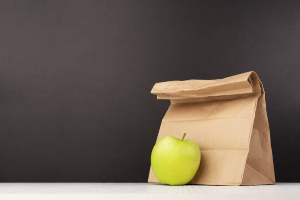 bolsa de almuerzo de papel marrón clásica con una manzana en el fondo de la pizarra para la escuela, paquete de desayuno simple y ecológico - packed lunch lunch paper bag blackboard fotografías e imágenes de stock