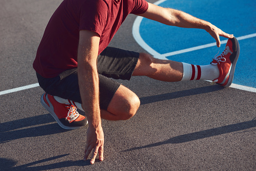 Man exercising and stretching on a public basket court in an urban park.