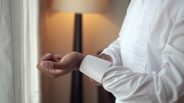 Elegant man getting dressed in the room. Groom buttoning his white shirt during his preparations for the wedding.